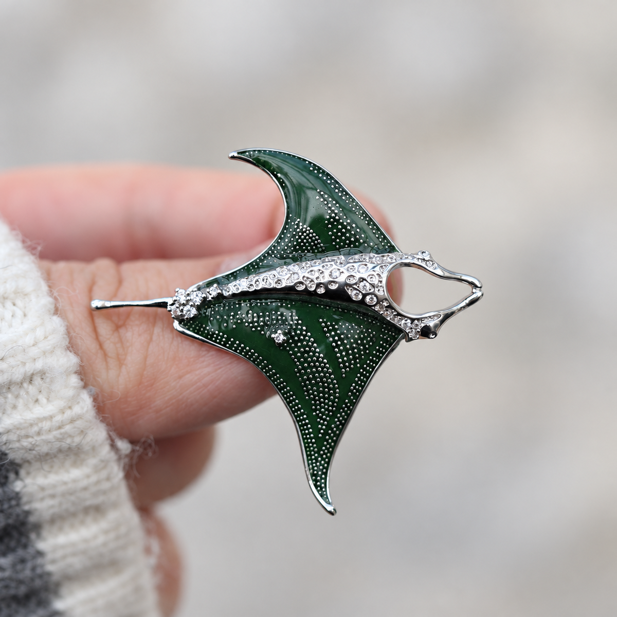 Green enamel manta ray brooch held in a hand