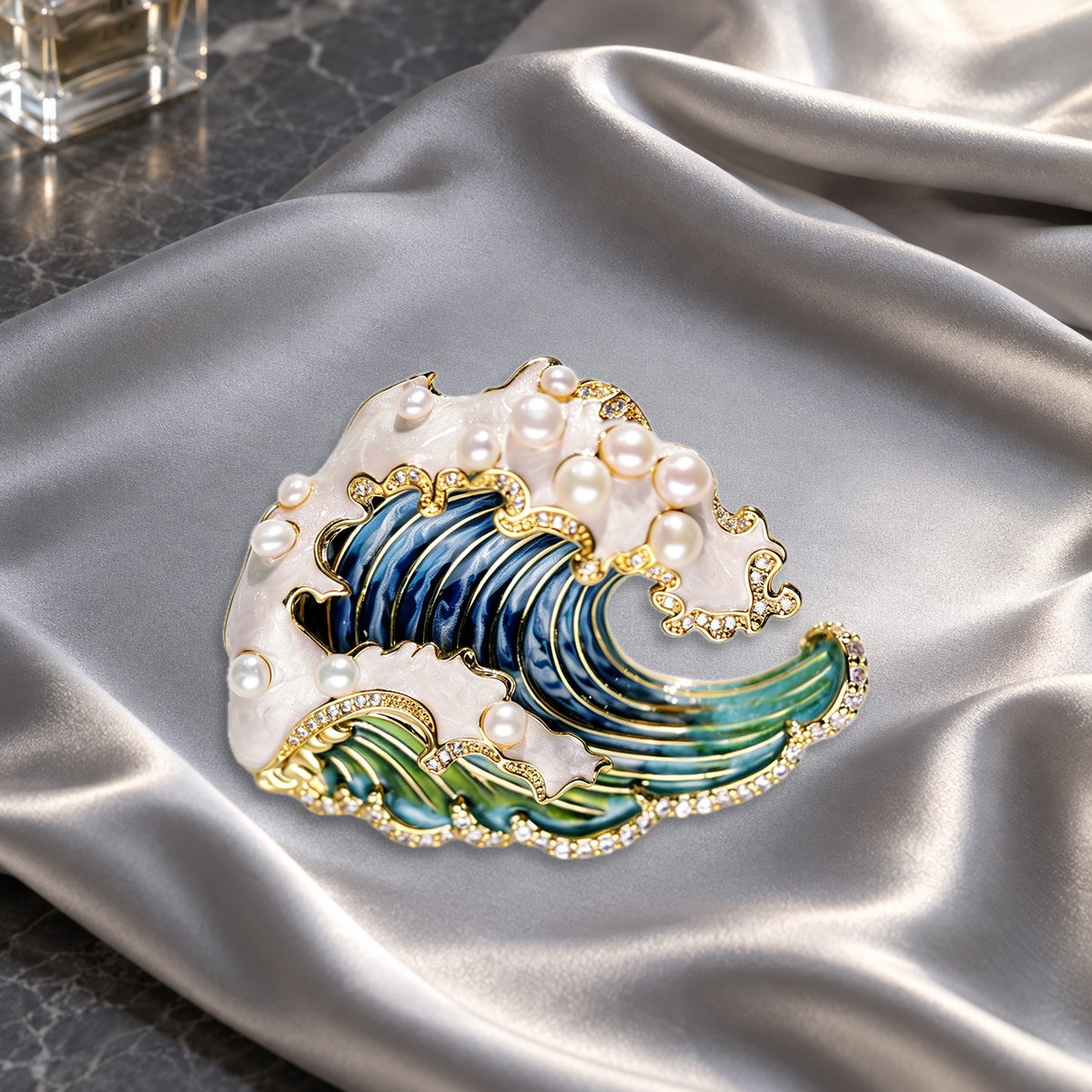Blue and green wave brooch with pearl accents on silver-gray satin on a dressing table.