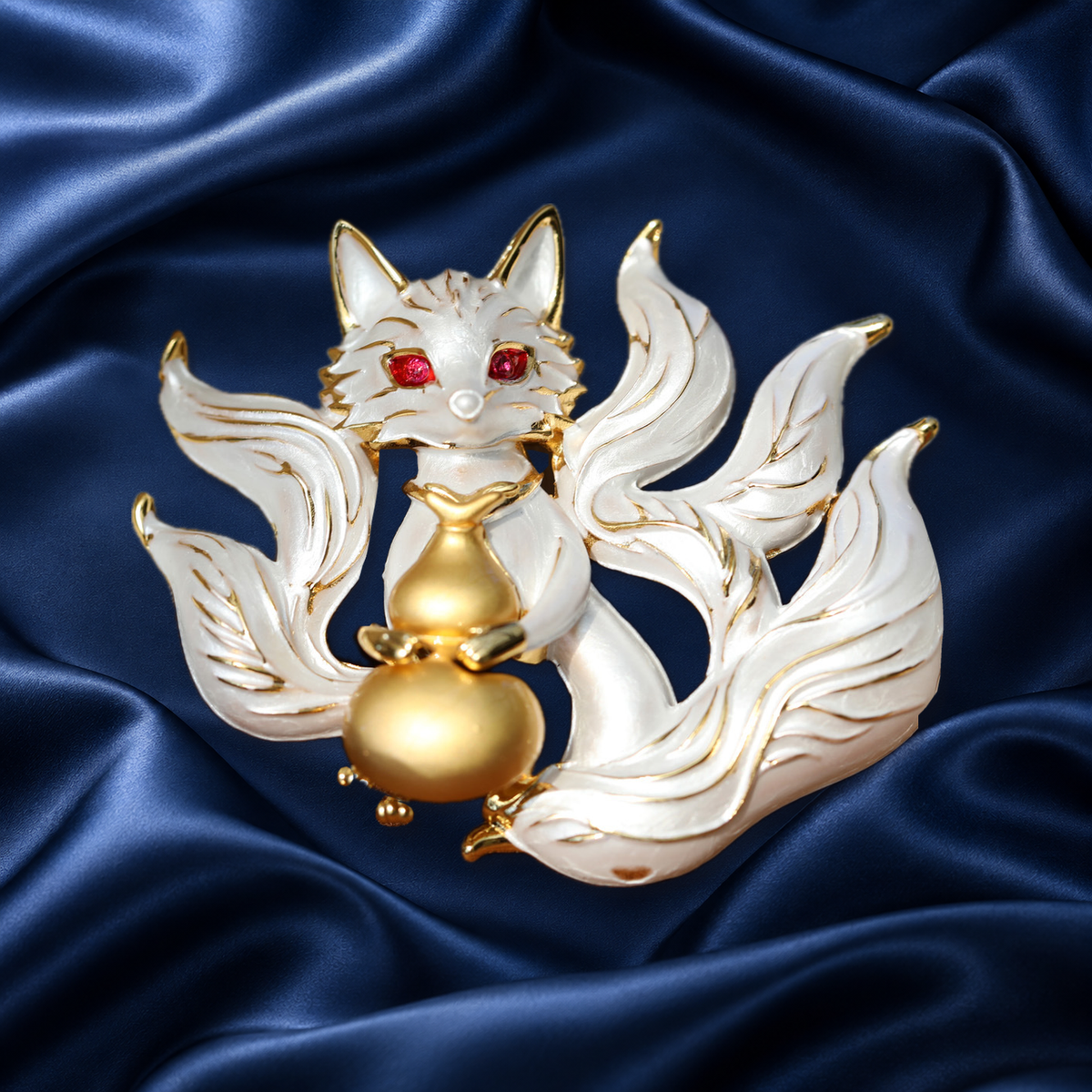 White enamel nine-tailed fox brooch with red eyes and a gold-tone gourd on navy satin