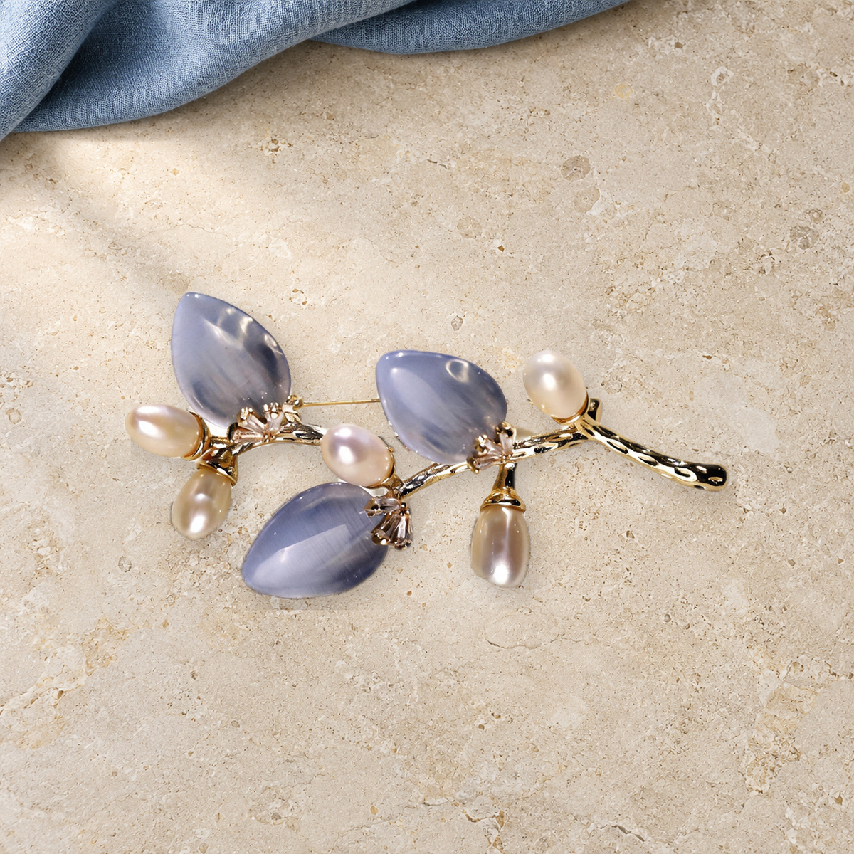 Blue cat-eye stone flower branch brooch with freshwater pearls in a styled tabletop scene