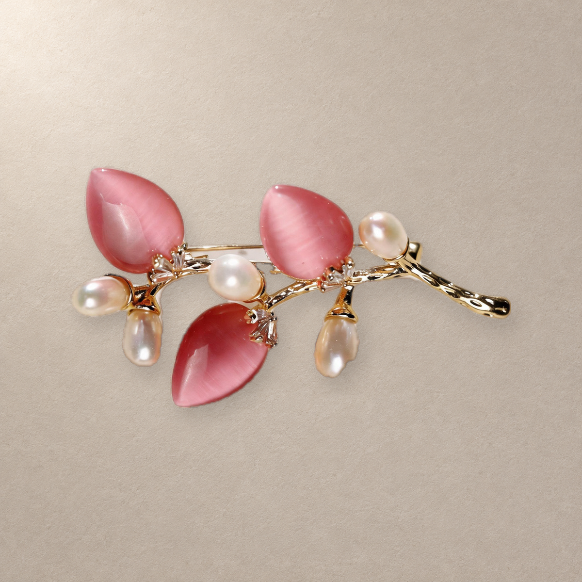 Pink cat-eye stone flower branch brooch with freshwater pearls on a neutral background