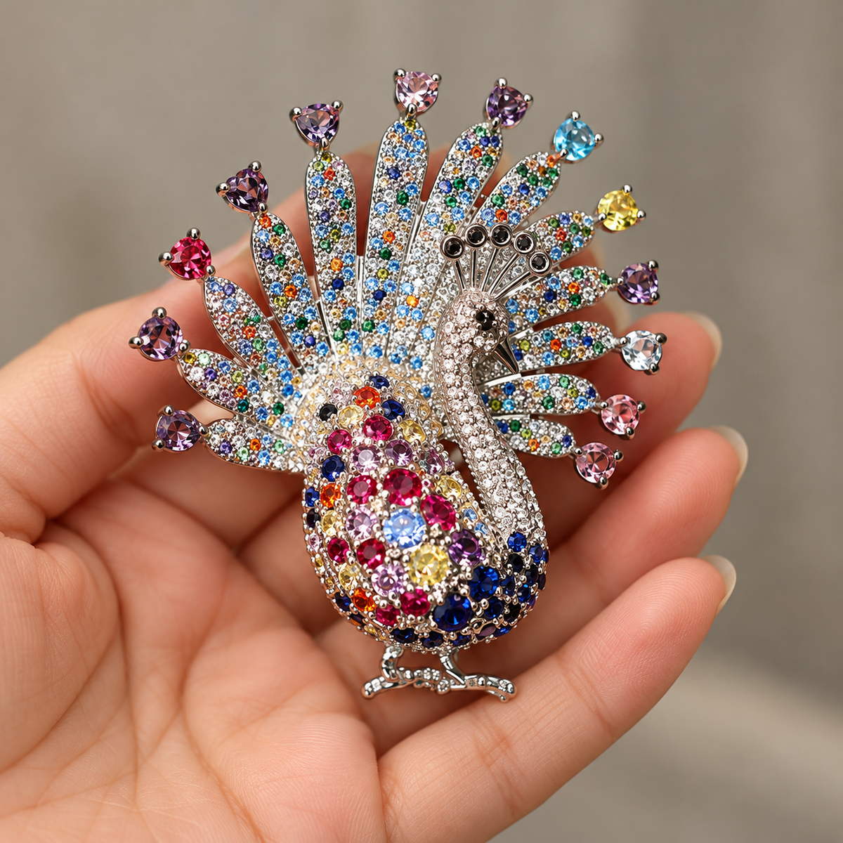 Silver-tone multicolor peacock brooch held in a hand