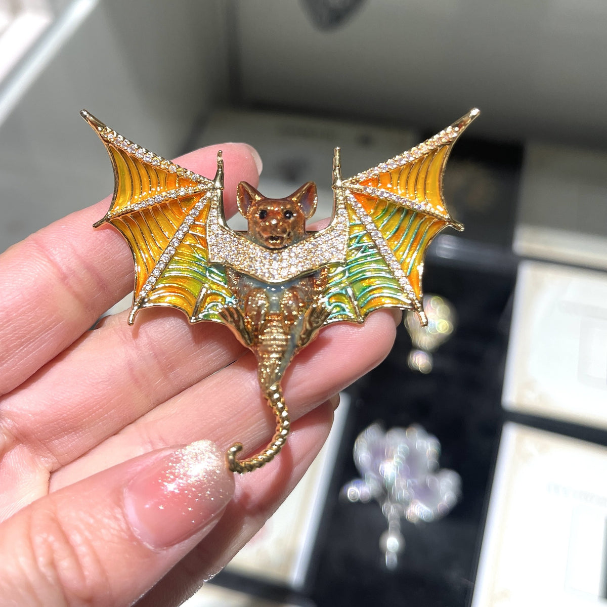 Colorful copper bat brooch with orange and green wings and curled tail, handheld view