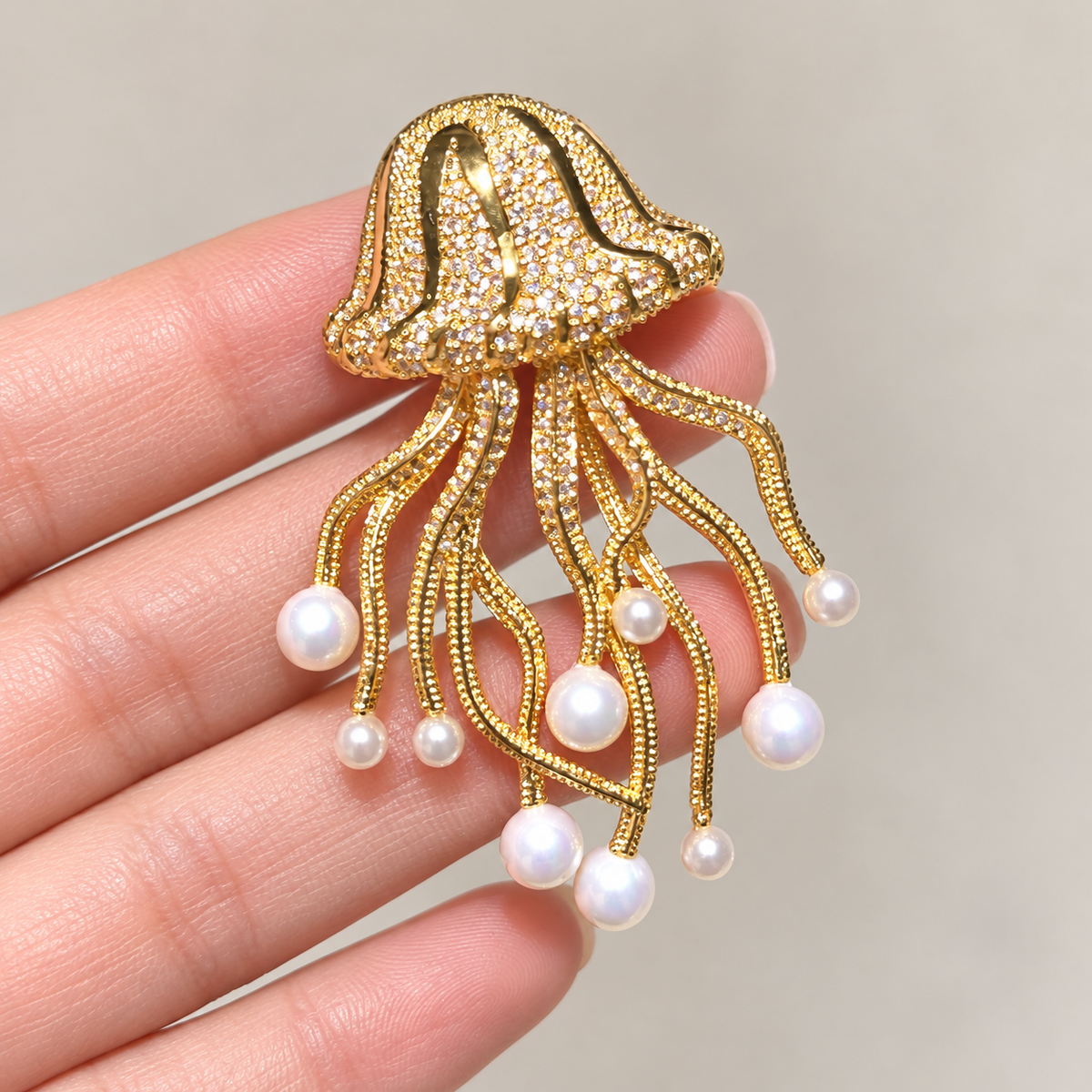 Gold-tone shell pearl jellyfish brooch held in a hand