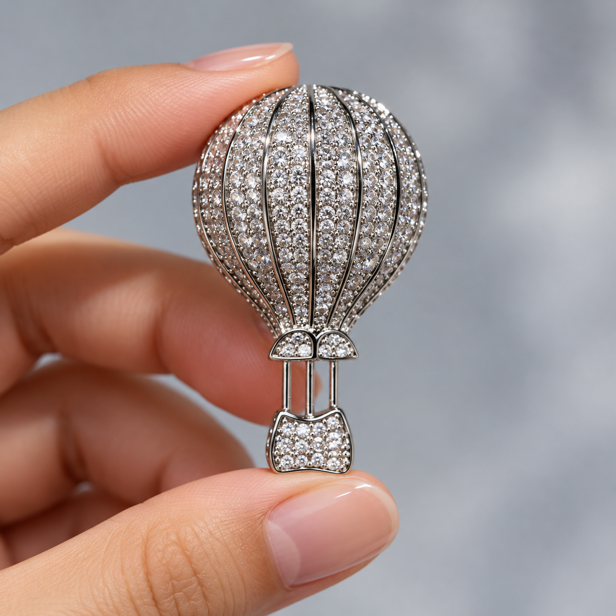 Silver hot air balloon brooch and pendant held in a hand