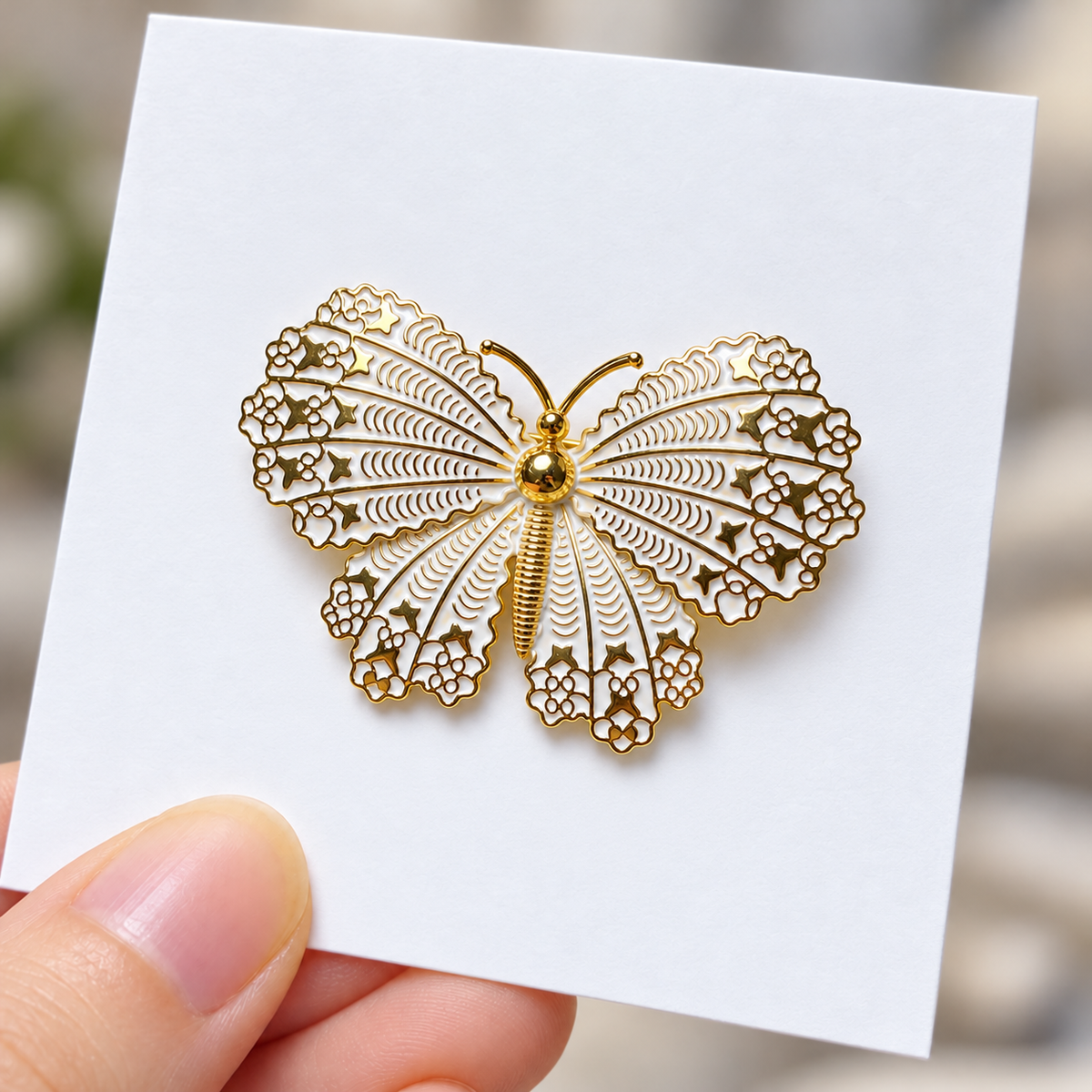 Gold tone and white butterfly brooch displayed on a card held in a hand