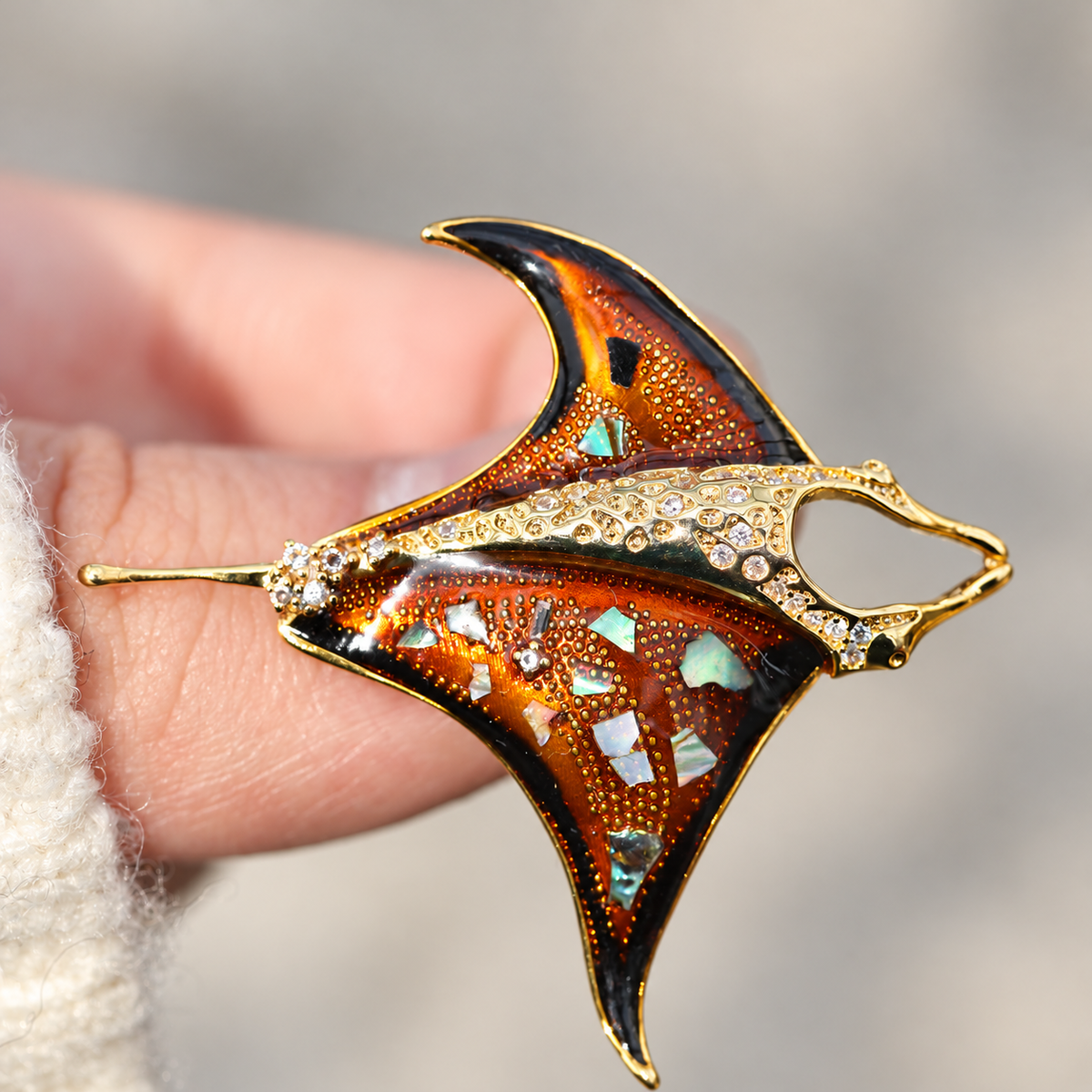 Orange enamel manta ray brooch held in a hand