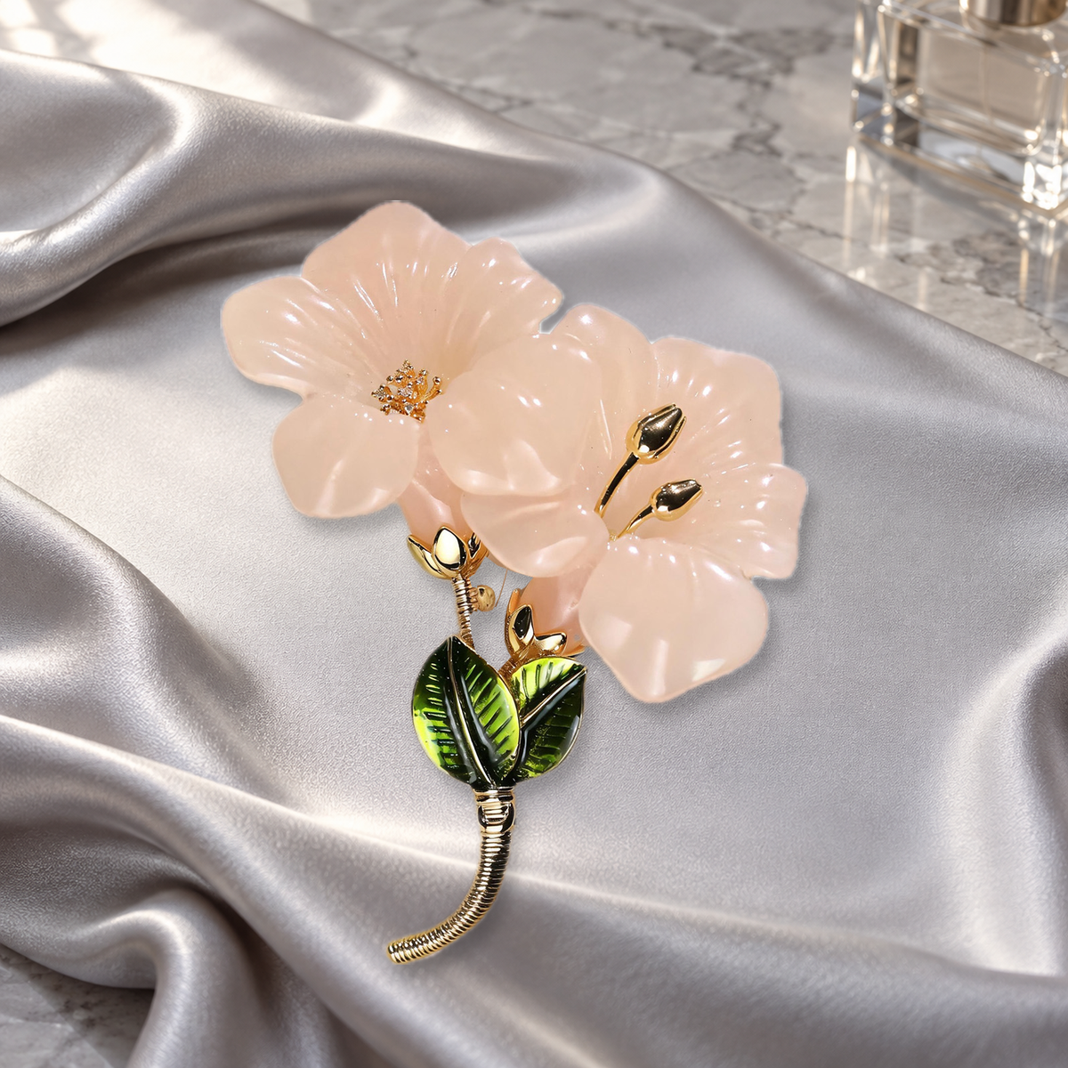 Pale pink flower brooch with a gold-tone center and green leaves on silver-gray satin on a dressing table.