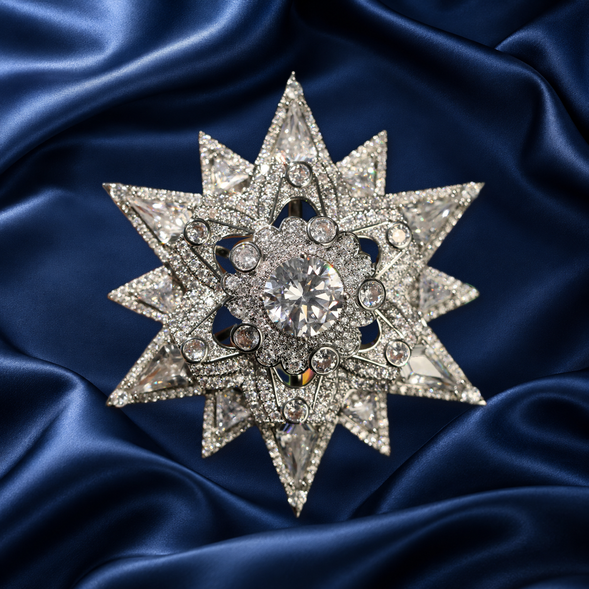 Silver-tone layered starburst brooch with a faceted center and sparkling accents on navy satin
