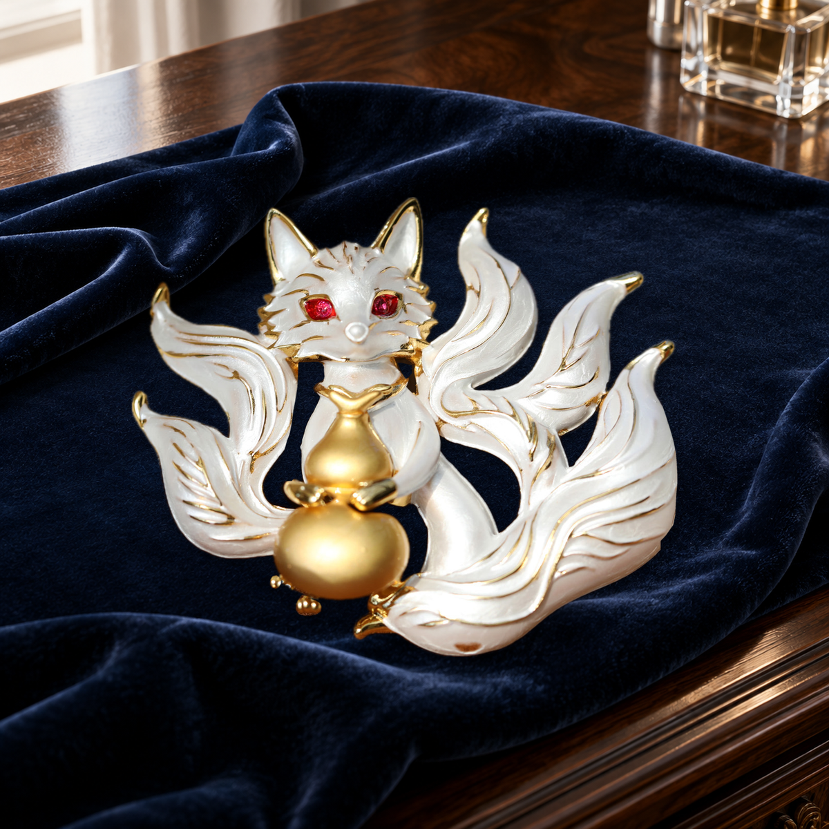 White enamel fox brooch with flowing tails and a gold-tone gourd on navy velvet on a dressing table.