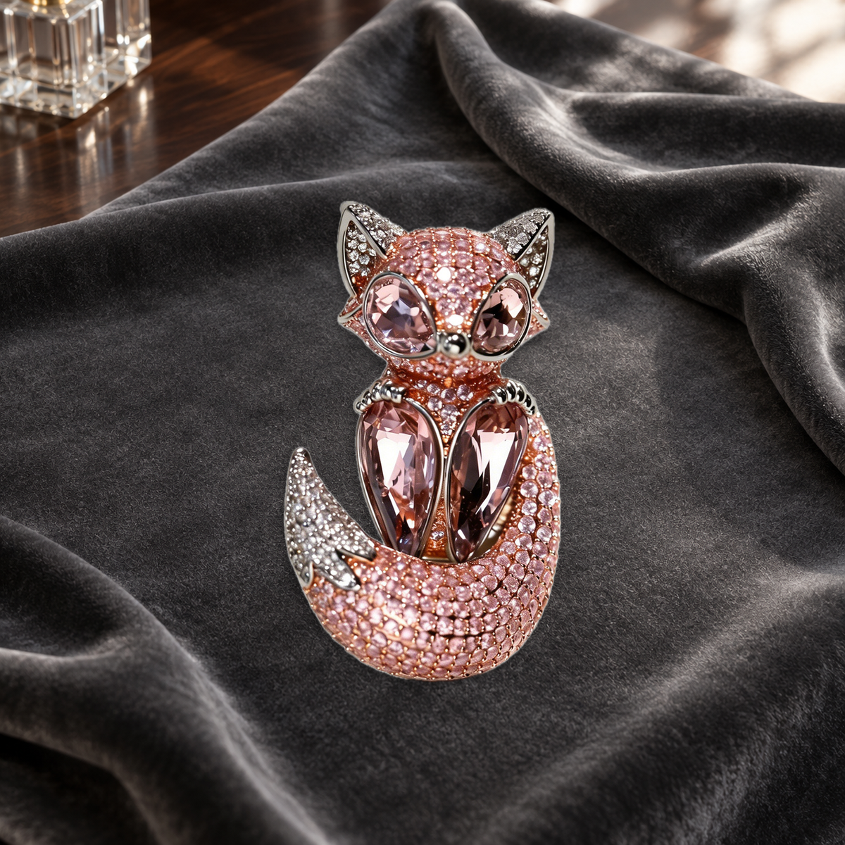 Pink fox brooch with faceted eyes and chest accents resting on charcoal velvet on a dressing table.
